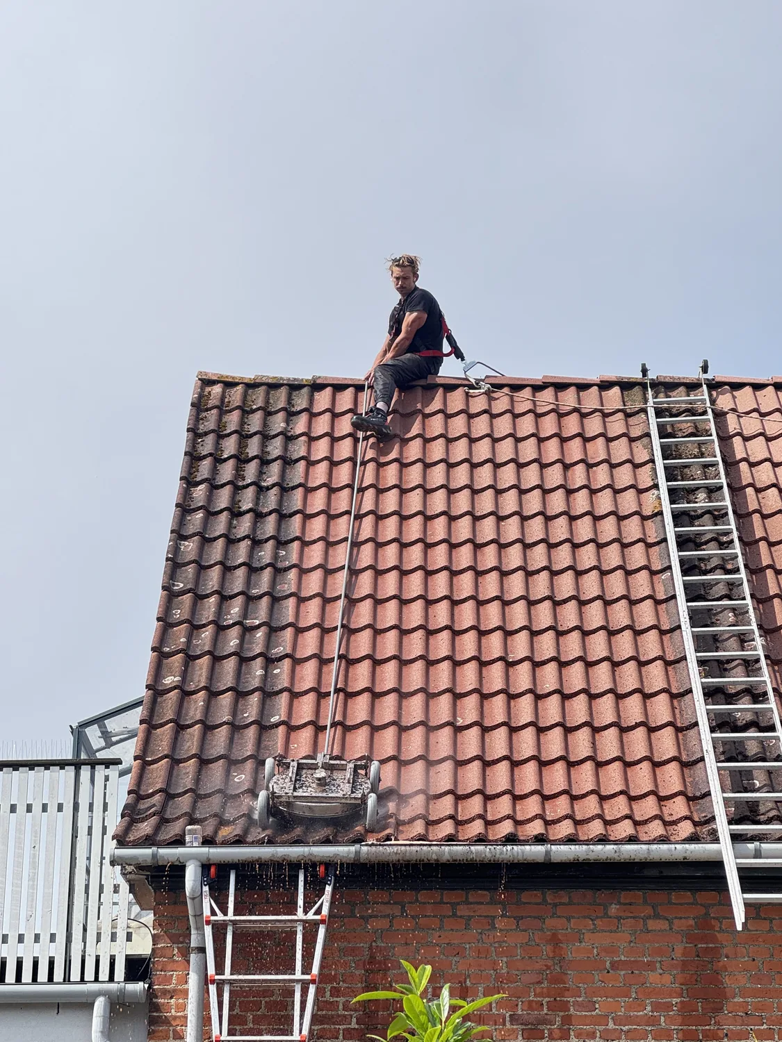 Roterende lavtryksrenser arbejder sig ned ad et rødt tegltag på en villa, mens medarbejderen styrer den fra tagryggen og vandet løber ned over stenene